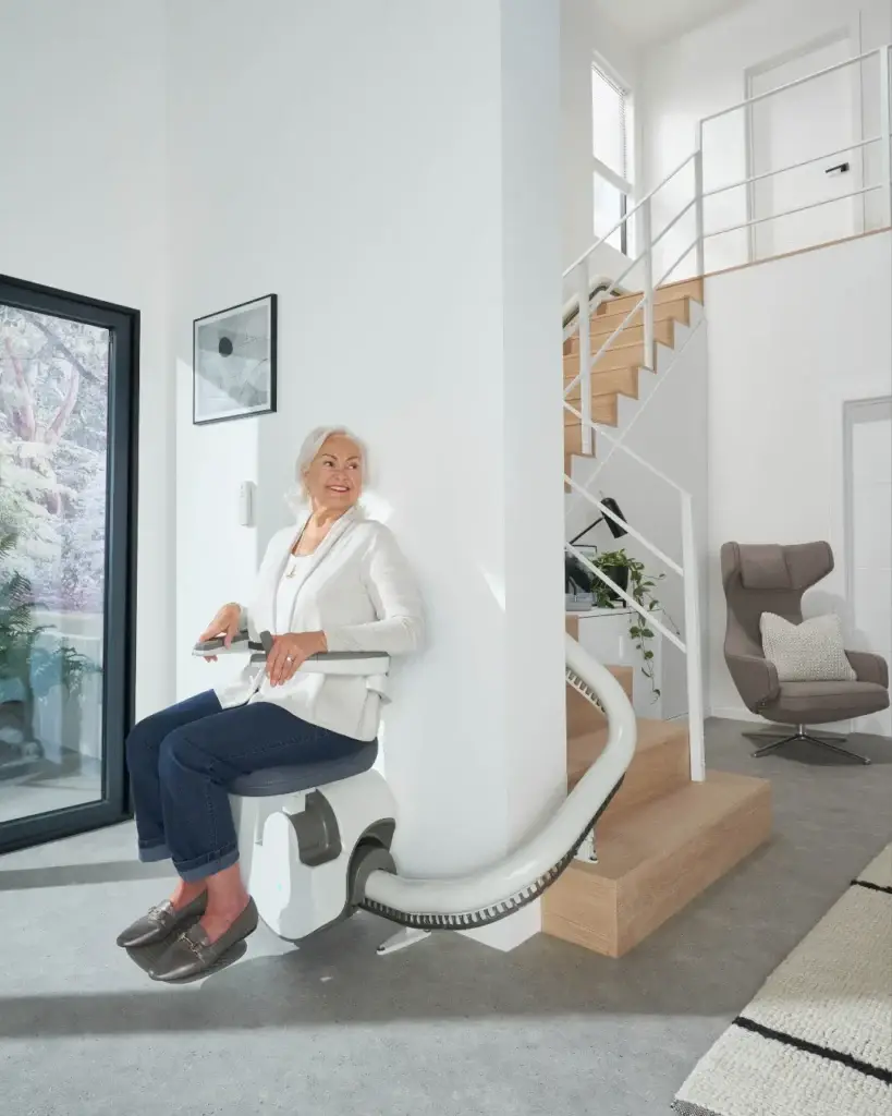 A woman seated on a Flow X stairlift beside a curved staircase